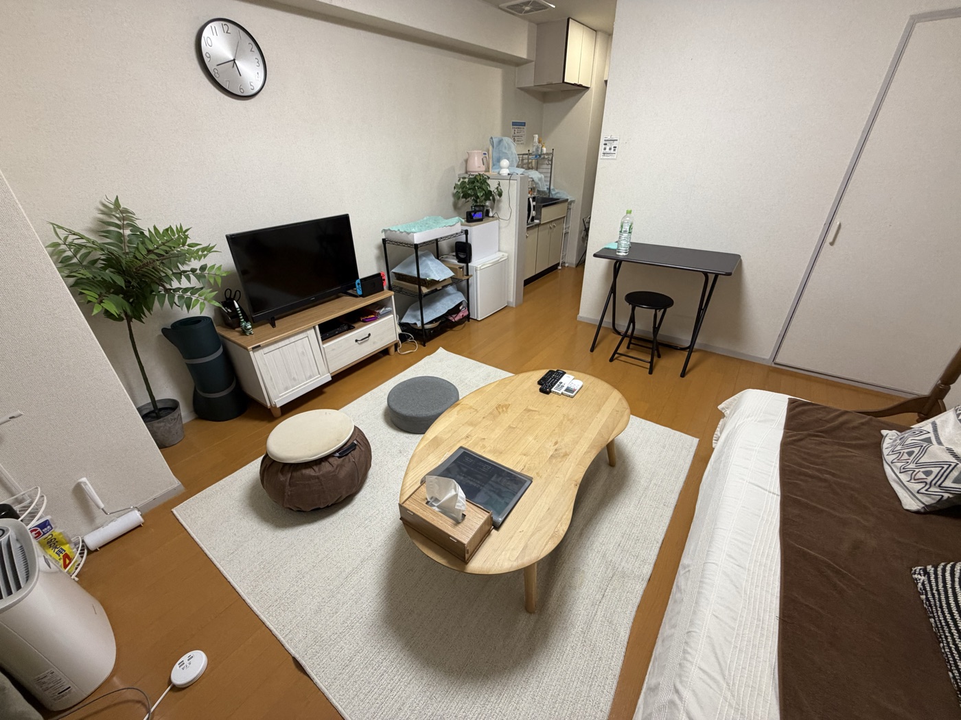 お気軽スペースHARU 武ステーションの室内。フローリングにラグと丸い座卓、クッション、テレビ、奥にミニキッチン