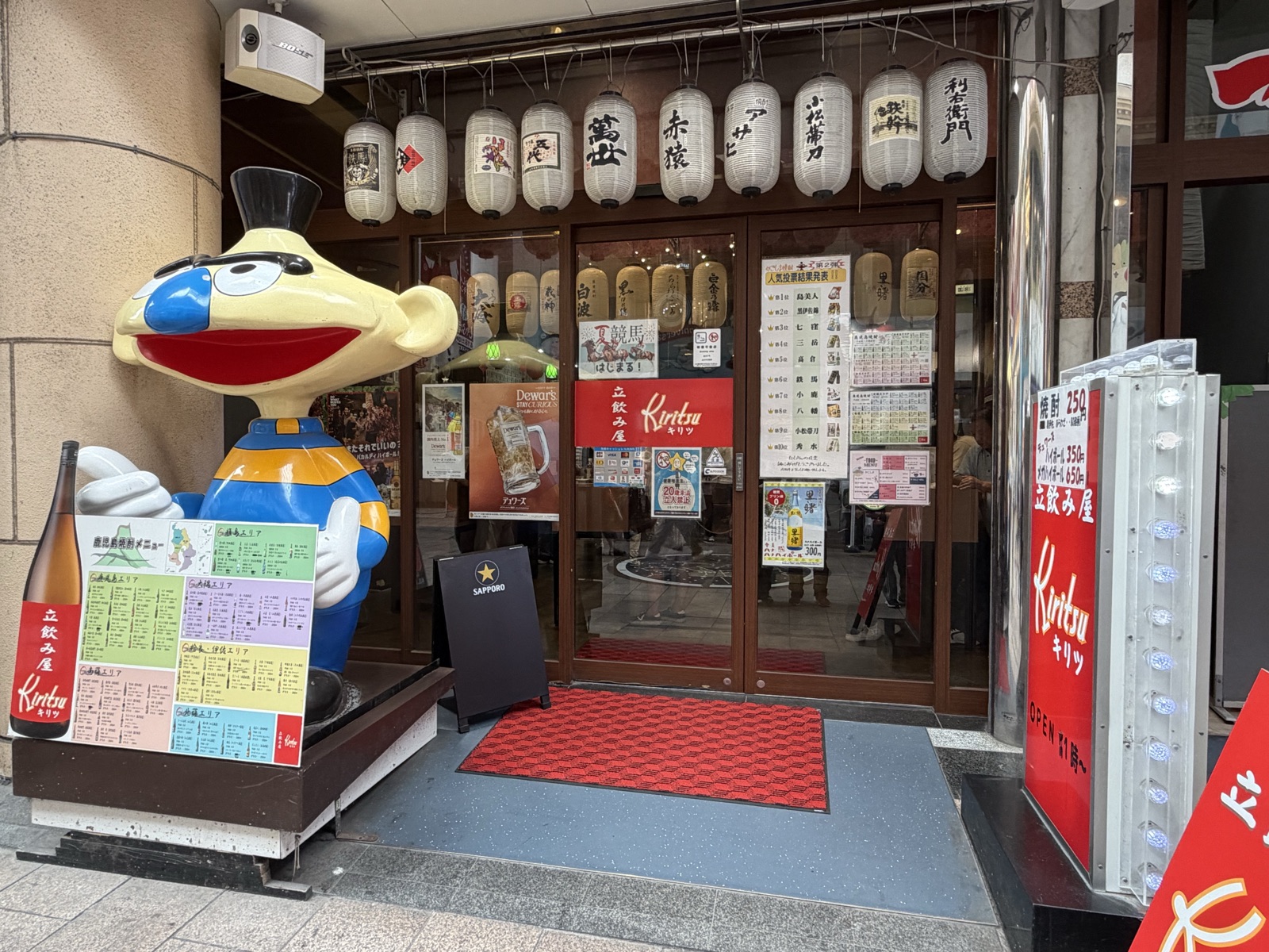 立飲み屋Kiritsu（キリツ）天文館店の入口。焼酎の提灯とエリア別焼酎メニューが並ぶ
